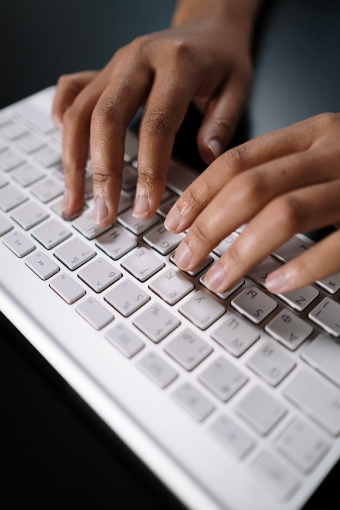 A close-up view of hands typing on a sleek white keyboard in a modern workspace.