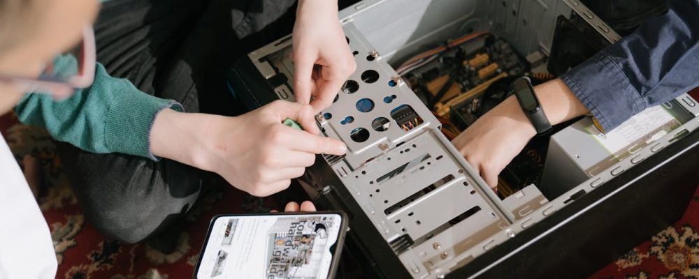 A close-up of hands fixing a computer with guidance from a mobile device.